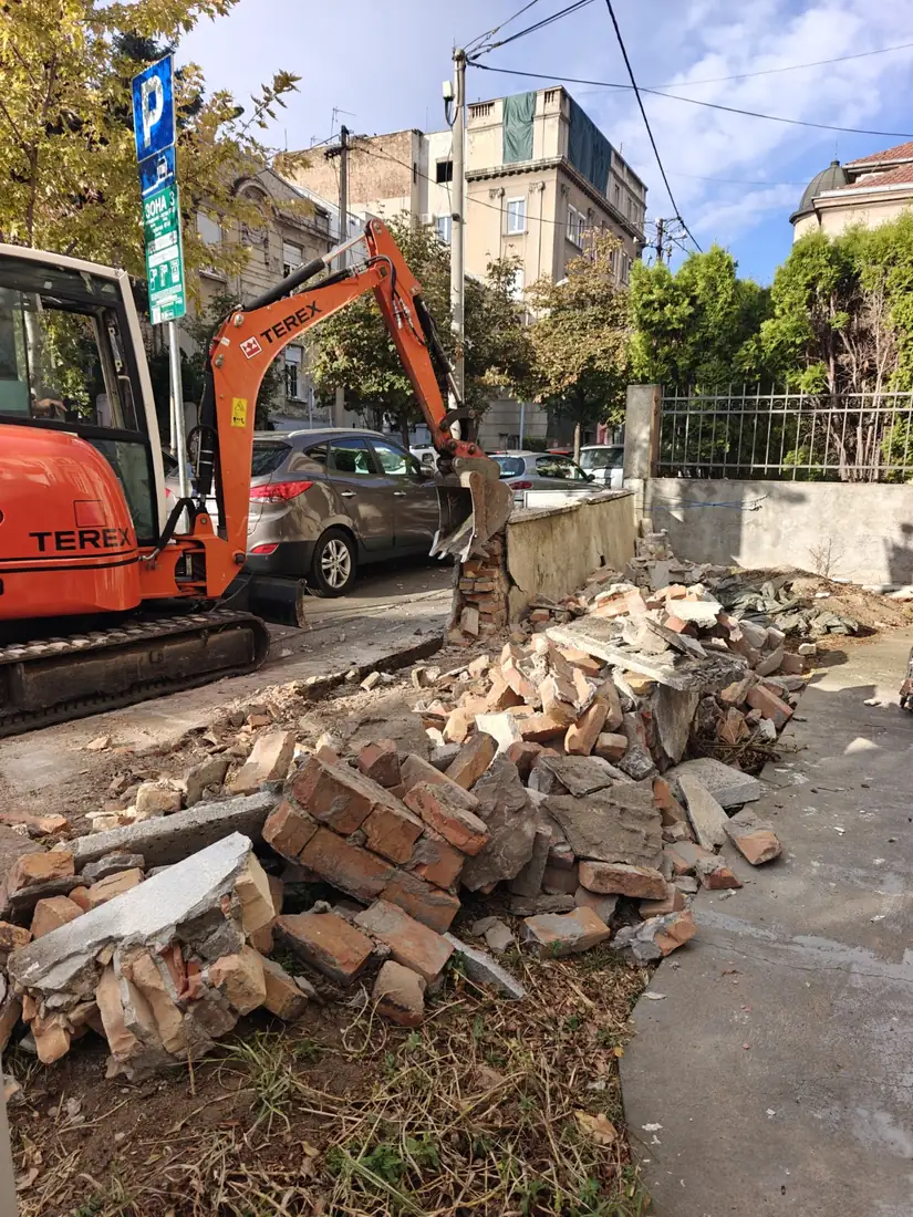 Mini-bager ruši staru zidanu ogradu, hrpa cigle i betonskog šuta